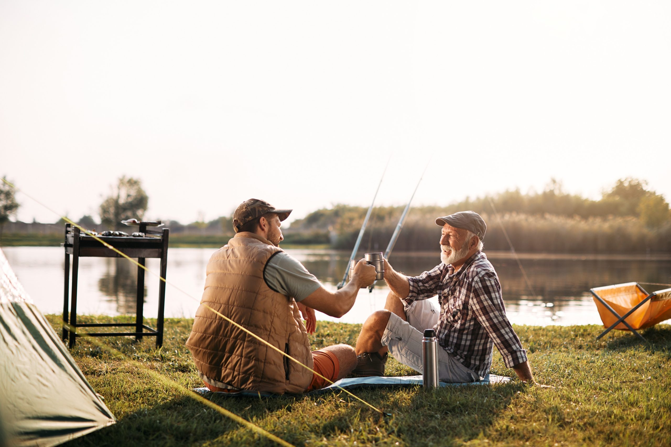 "Father and son toasting with beverages while fishing in a boat on a lake at sunset"